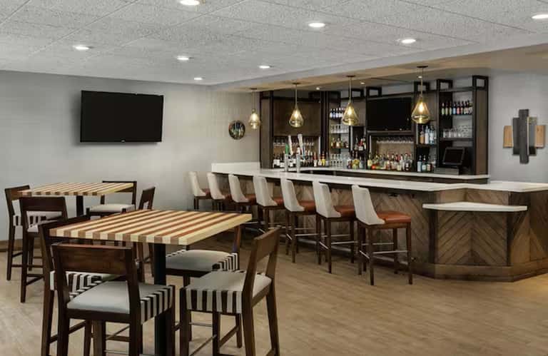 Casual dining area with striped tables, wood bar with pendant lights, and flat-screen TV