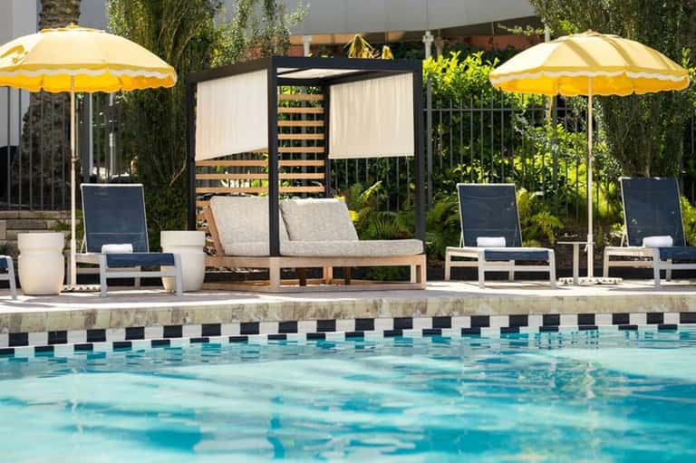 Resort pool with lounge chairs, yellow umbrellas, and modern pergola with lush green landscaping