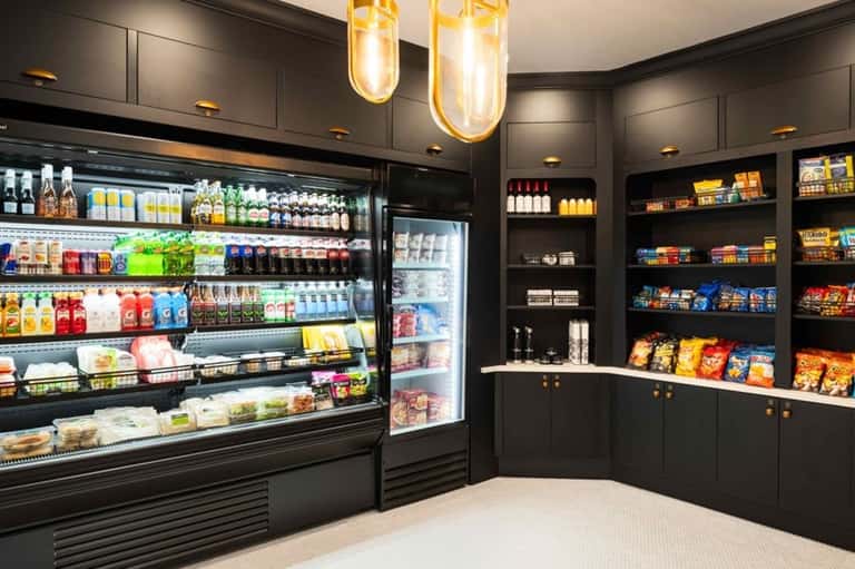 Modern convenience store with black cabinetry, refrigerated display cases, shelving with snacks and beverages, and pendant lighting