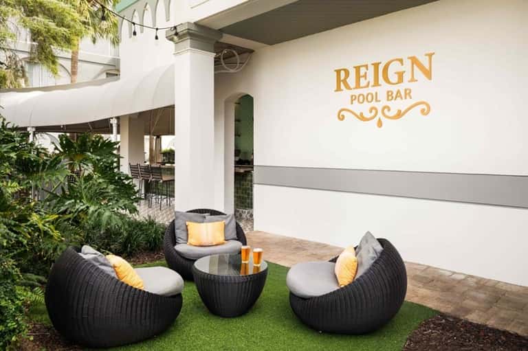 Reign Pool Bar outdoor lounge with black wicker seating, cushions, and tropical landscaping