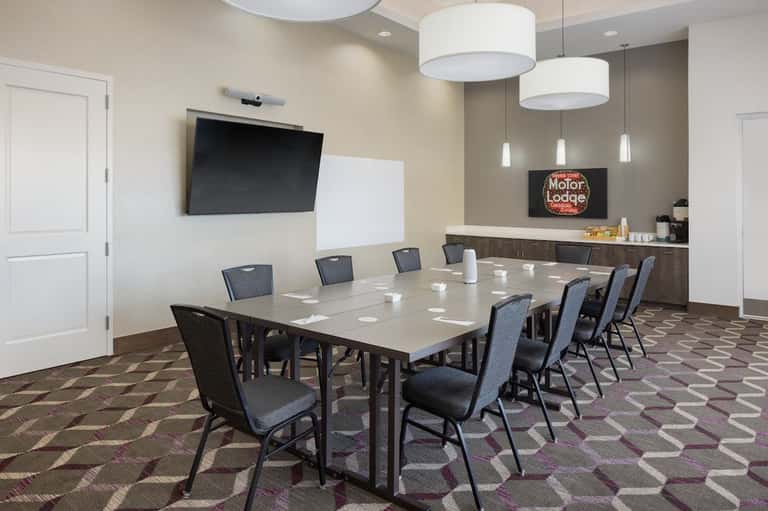 Hotel conference room with rectangular table, blue chairs, wall-mounted TV, and service counter