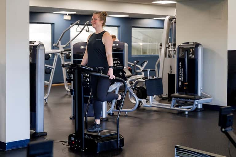 Gym interior with woman on stationary bike, surrounded by cardio and strength training equipment