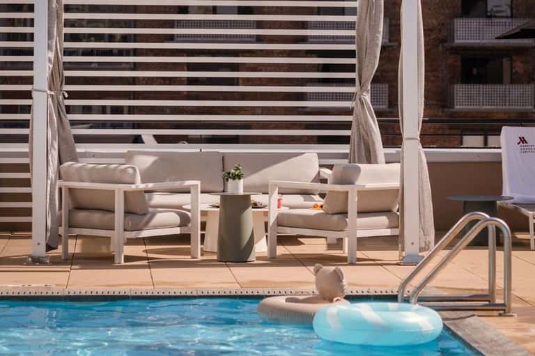 Luxury poolside lounge area with white chairs, umbrellas, and a person floating on an inflatable in the pool