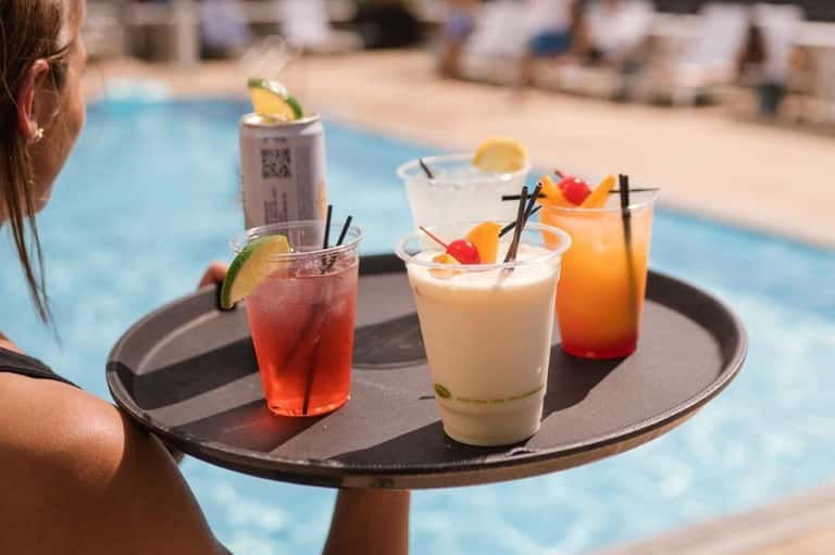 Server holding a tray of colorful cocktails by the poolside during daytime at a resort