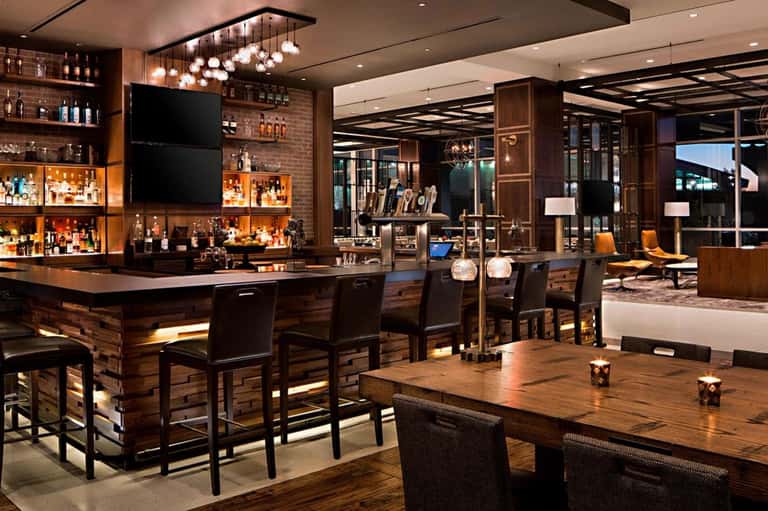 Modern hotel bar and lounge interior with wood accents, illuminated shelving, and contemporary seating