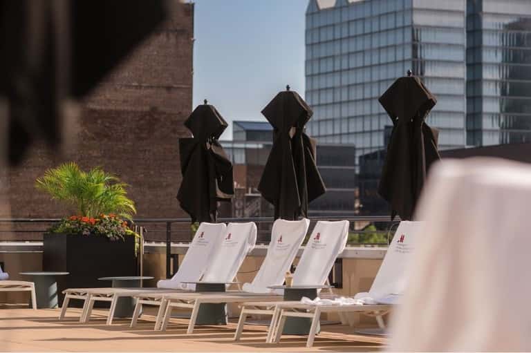 Rooftop terrace with white lounge chairs, black umbrellas, and city skyline views with brick buildings