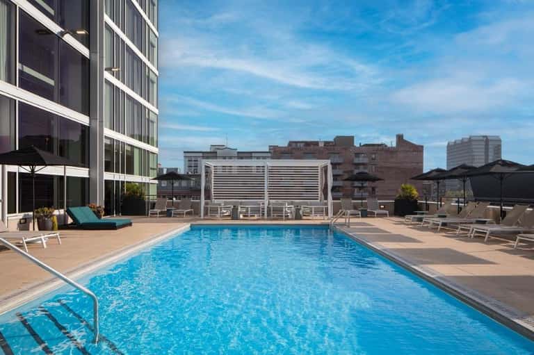 Resort outdoor swimming pool with blue water, lounge chairs, umbrellas, and modern building exterior