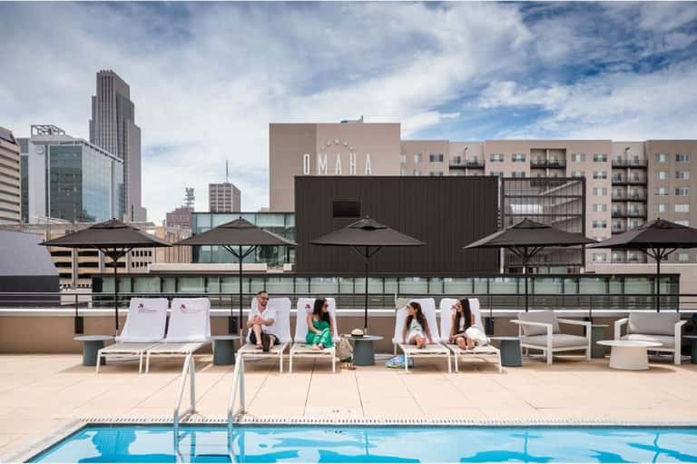 Rooftop pool deck with lounge chairs and umbrellas overlooking Omaha skyline during daytime