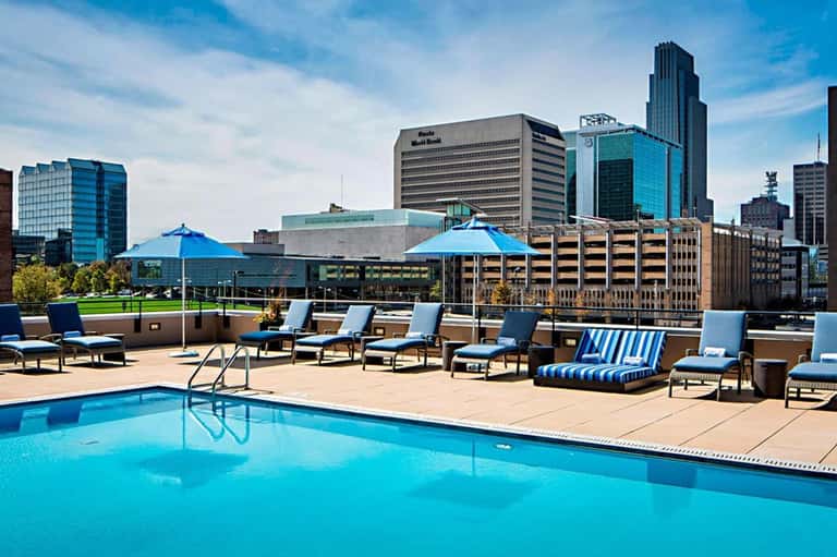 Outdoor pool with blue umbrellas and lounge chairs with downtown city views