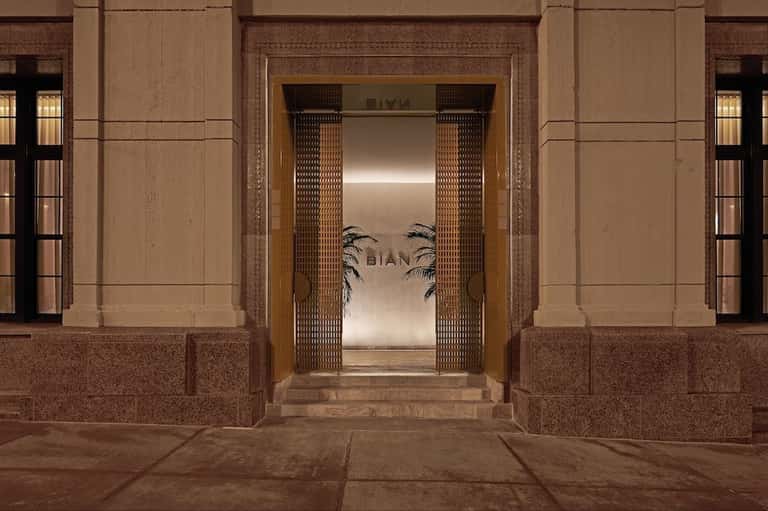 Elegant entrance to BIAN with ornate wooden doors, brass detailing, and neutral stone architectural framing