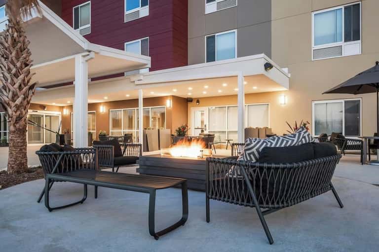 Outdoor courtyard patio with firepit, modern seating, pergola, and lit building facade at night