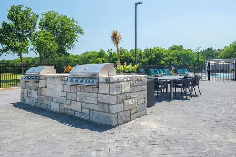 Outdoor grilling station with stone base, two gas grills, dining table, and resort grounds beyond