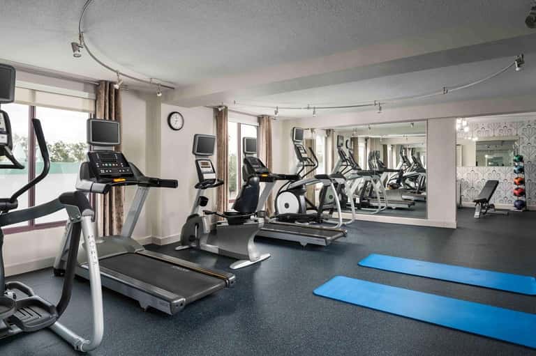 Modern fitness center with treadmills, exercise bikes, mirrors, and blue yoga mats on dark flooring