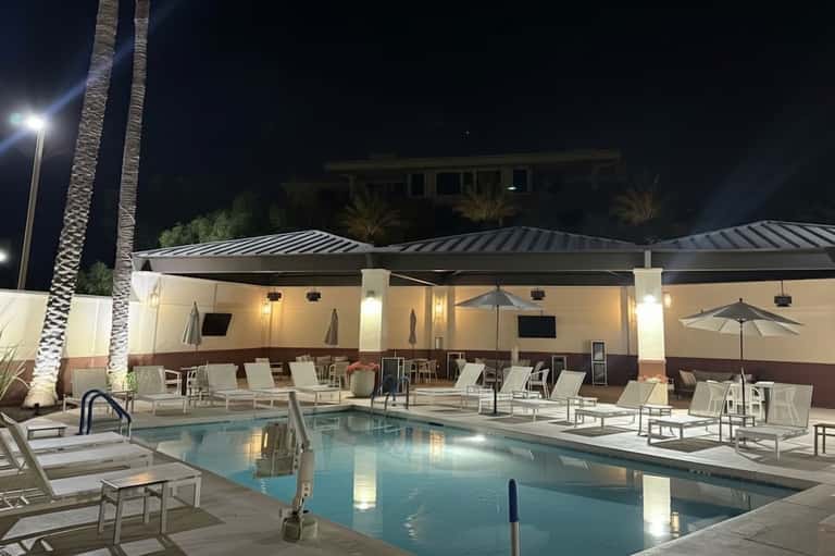 Nighttime pool area with illuminated cabana and lounge chairs under palm trees