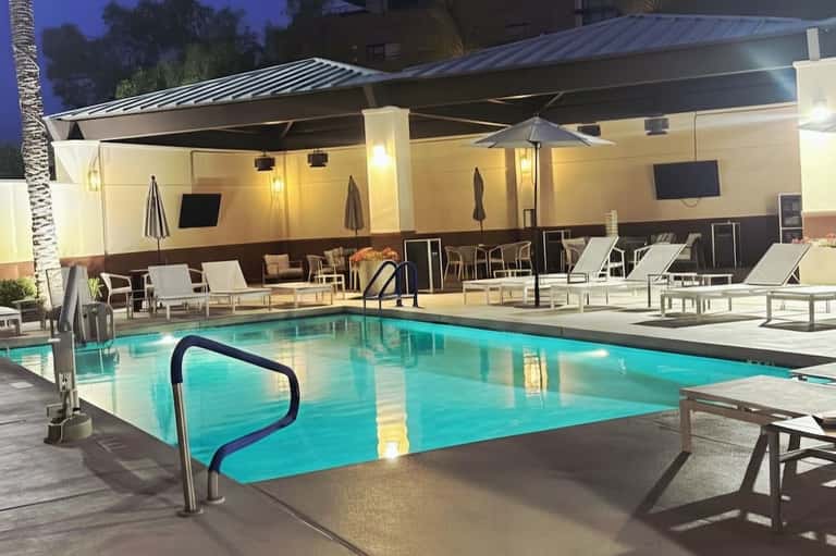 Evening pool deck with metal roof structure, umbrellas, and ambient lighting