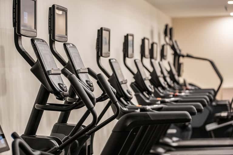 Row of elliptical machines with digital displays lined against a white wall in a gym