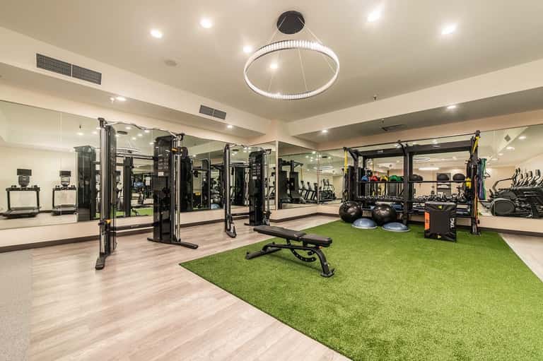 Modern fitness center with equipment, mirrors, green turf area, and circular pendant lighting