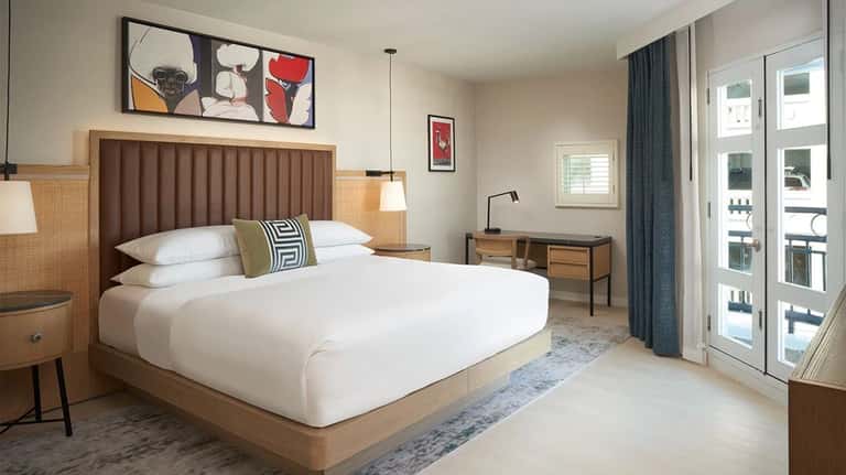 Spacious hotel bedroom with brown leather headboard, white bedding, and glass patio door
