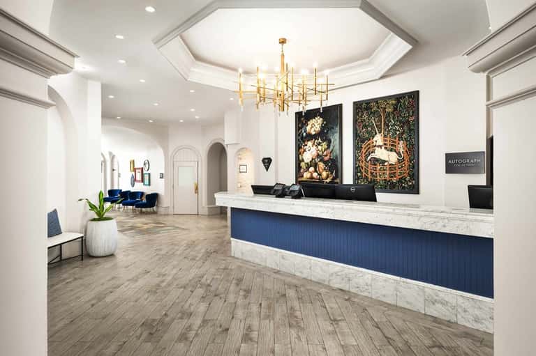 Modern hotel lobby with marble reception desk, gold chandelier, and blue velvet seating area