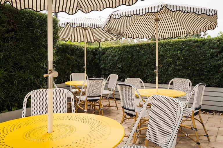 Outdoor patio dining area with yellow umbrellas, white chairs, and green hedges