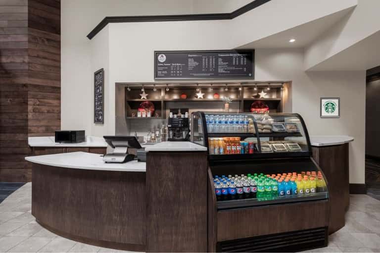 Modern Starbucks café counter with curved dark wood design, beverage cooler, menu board, and white marble countertops