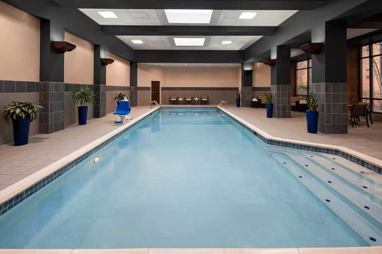 Indoor lap pool facility with slate tile accents, columns, pale walls, and blue poolside chair