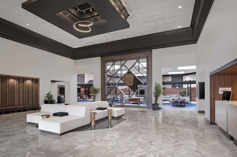 Luxury hotel lobby with white marble floors, dark wood ceiling details, and contemporary furniture
