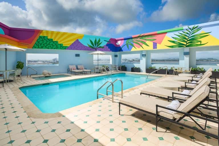 Rooftop indoor pool with colorful geometric ceiling mural and waterfront views, lounge seating
