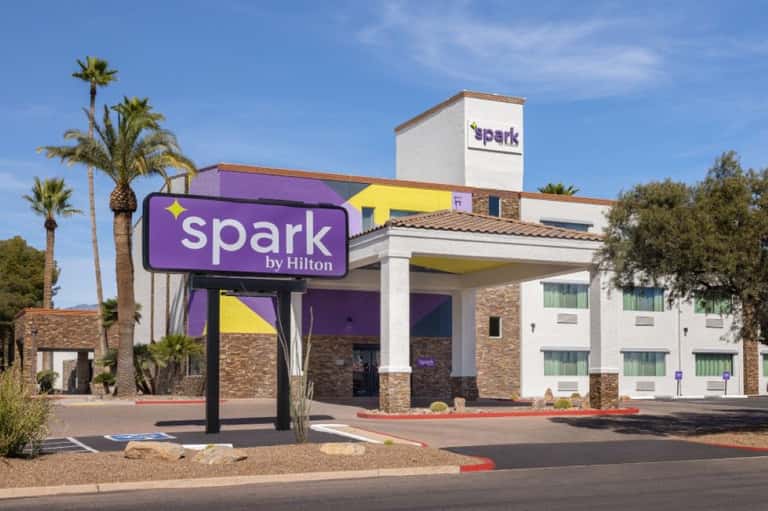 Spark by Hilton hotel exterior with purple and yellow signage and palm tree landscaping