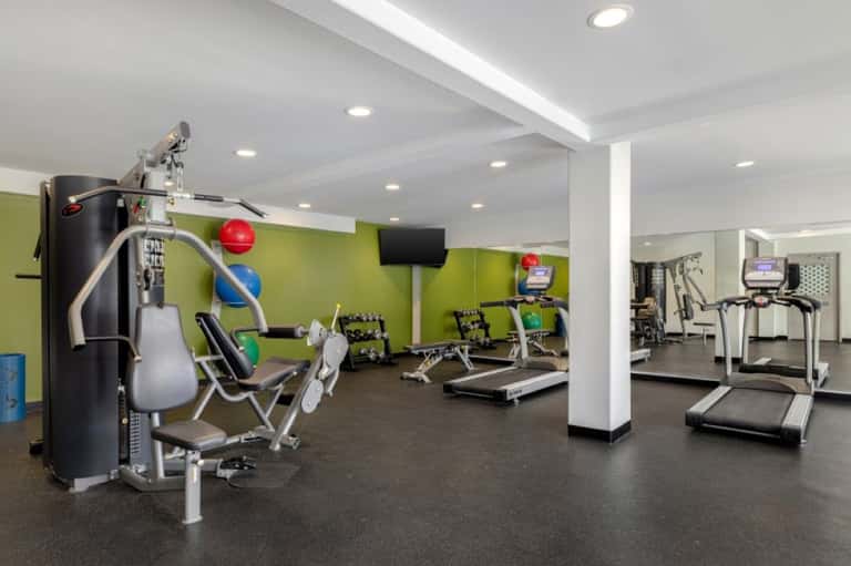 Hotel fitness center with cardio equipment, exercise machines, lime green wall, and recessed lighting