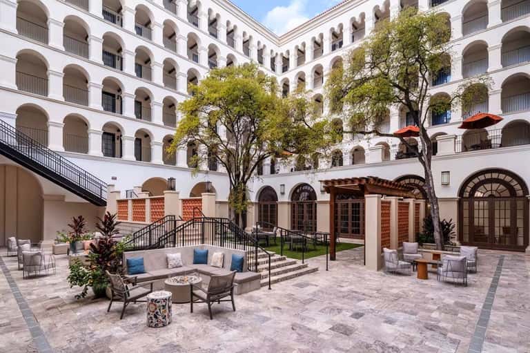 Elegant courtyard with white arched colonnade, mature trees, lounging areas, and terracotta pergola structures