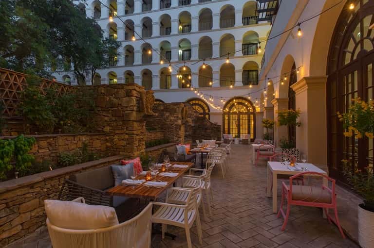 Evening dining courtyard with stone walls, string lights, tables set for service, and historic building backdrop