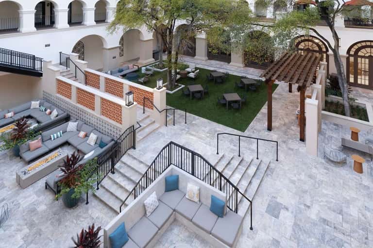 Multi-level courtyard with seating areas, fire pit, green lawn, mature trees, and white architectural elements