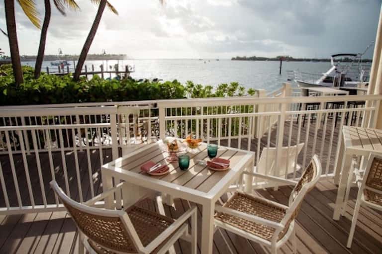 Waterfront balcony with dining table, white railings, bay views, and palm trees