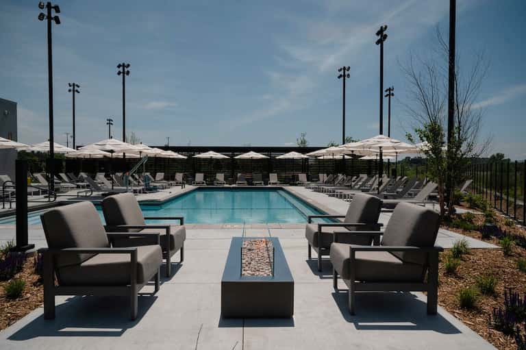Resort pool with linear fire pit, gray lounge chairs, white umbrellas, and manicured grounds