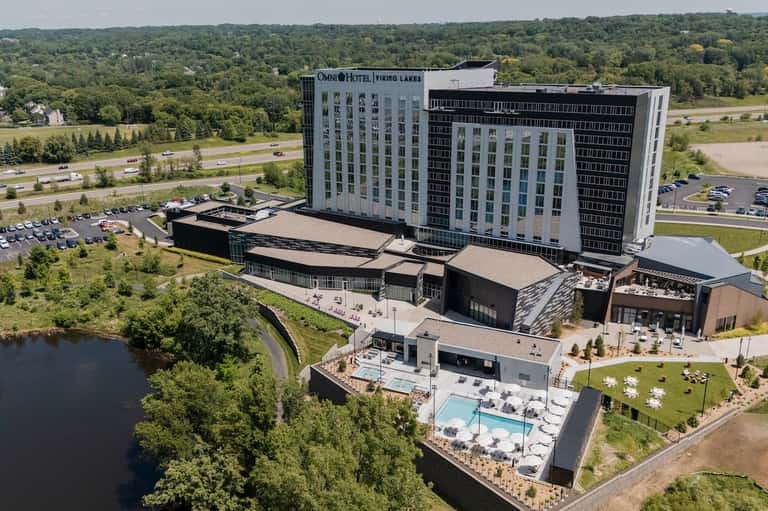 Aerial view of Omni Hotel Viking Lakes with pool deck, building tower, and surrounding green landscape