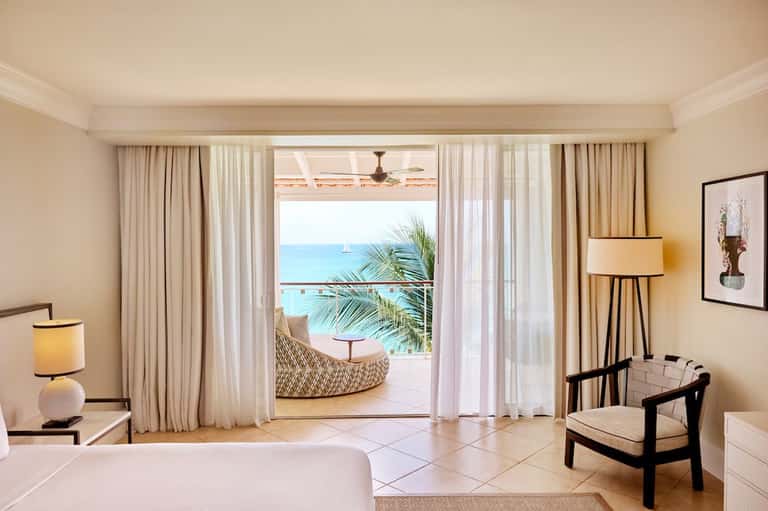 Luxury beachfront hotel room with ocean view terrace, elegant furnishings, and direct access to white sand beach