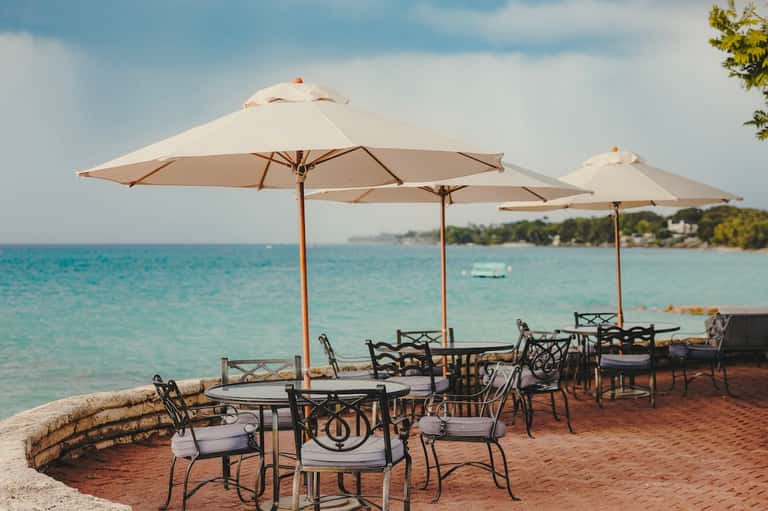 Beachside dining area with cream umbrellas, metal chairs, and turquoise water views