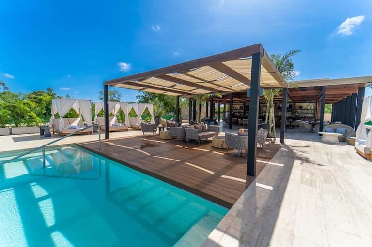 Luxurious outdoor pool area with wooden deck, pergola shade structure, lounge seating, and bar area