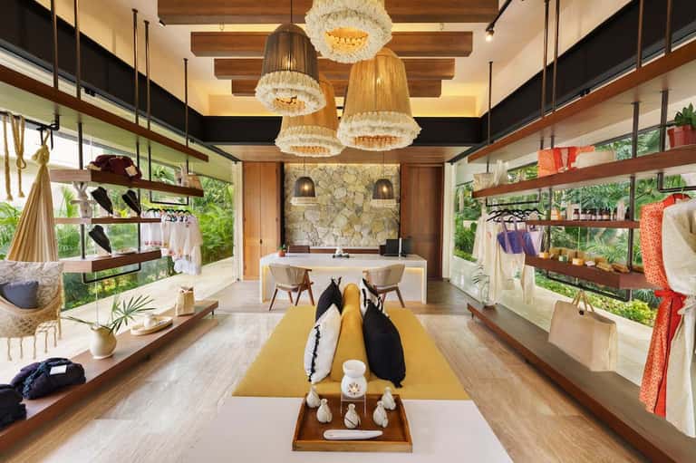 Modern boutique retail space with wooden shelving, pendant lighting, and natural greenery views