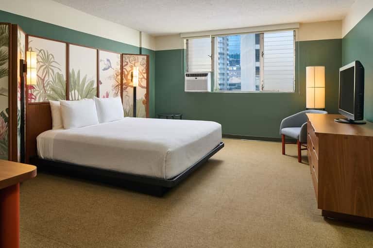 Contemporary hotel room with teal accent wall, queen bed, desk, and city views