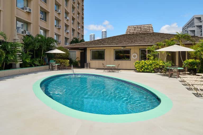 Resort swimming pool with turquoise deck surround, cabana building, and tropical landscaping