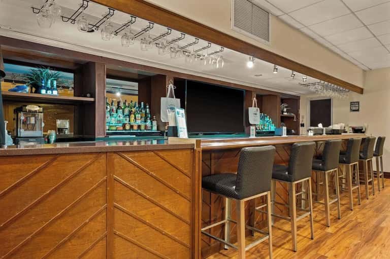 Hotel bar counter with wood cabinetry, turquoise accents, bar stools, and shelves of liquor bottles