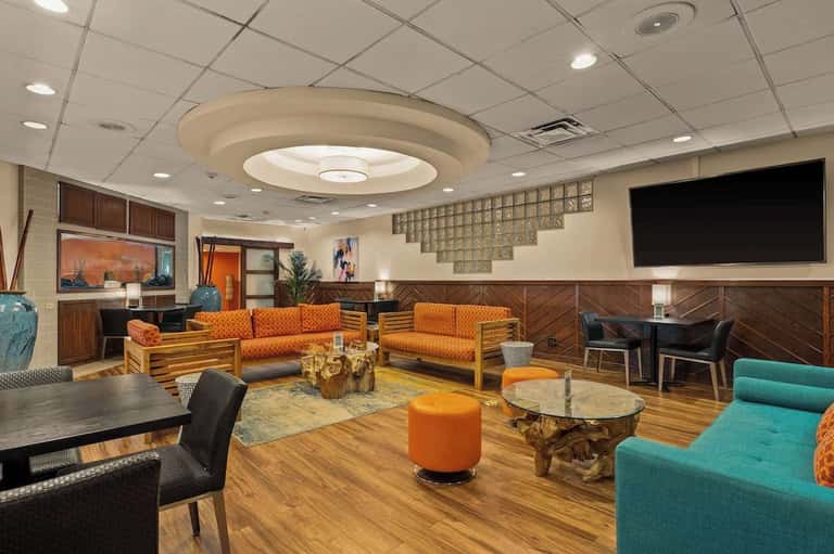 Modern hotel lobby lounge with orange and turquoise furniture, wood accents, and decorative ceiling detail
