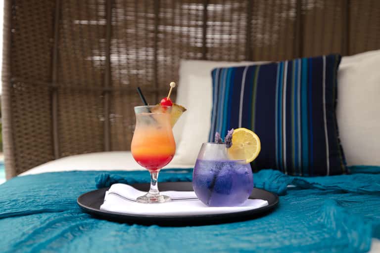 Colorful cocktails on tray inside woven egg chair with striped pillows and white bedding