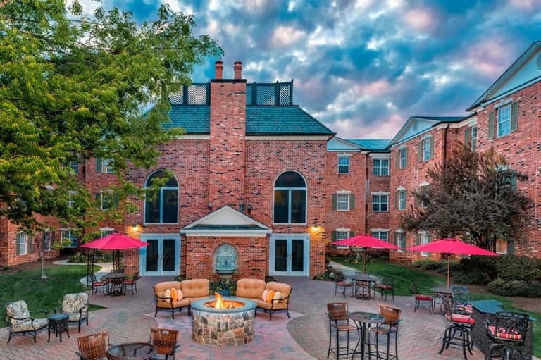 Brick hotel courtyard with firepit, orange chairs, pink umbrellas, and evening lighting