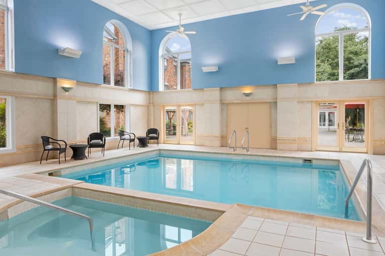 Indoor heated swimming pool with blue walls, white trim, lounge chairs, and large windows