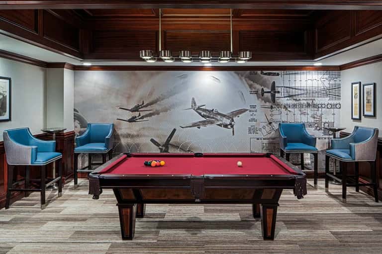 Game room with billiards table, red felt, aviation-themed wallpaper, blue chairs