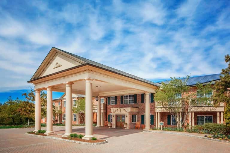 Brick hotel exterior with white columns, portico entrance, landscaping, and blue sky