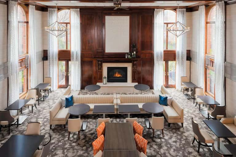 Elegant hotel lobby with fireplace, wooden beams, cream seating, blue accents, symmetrical design